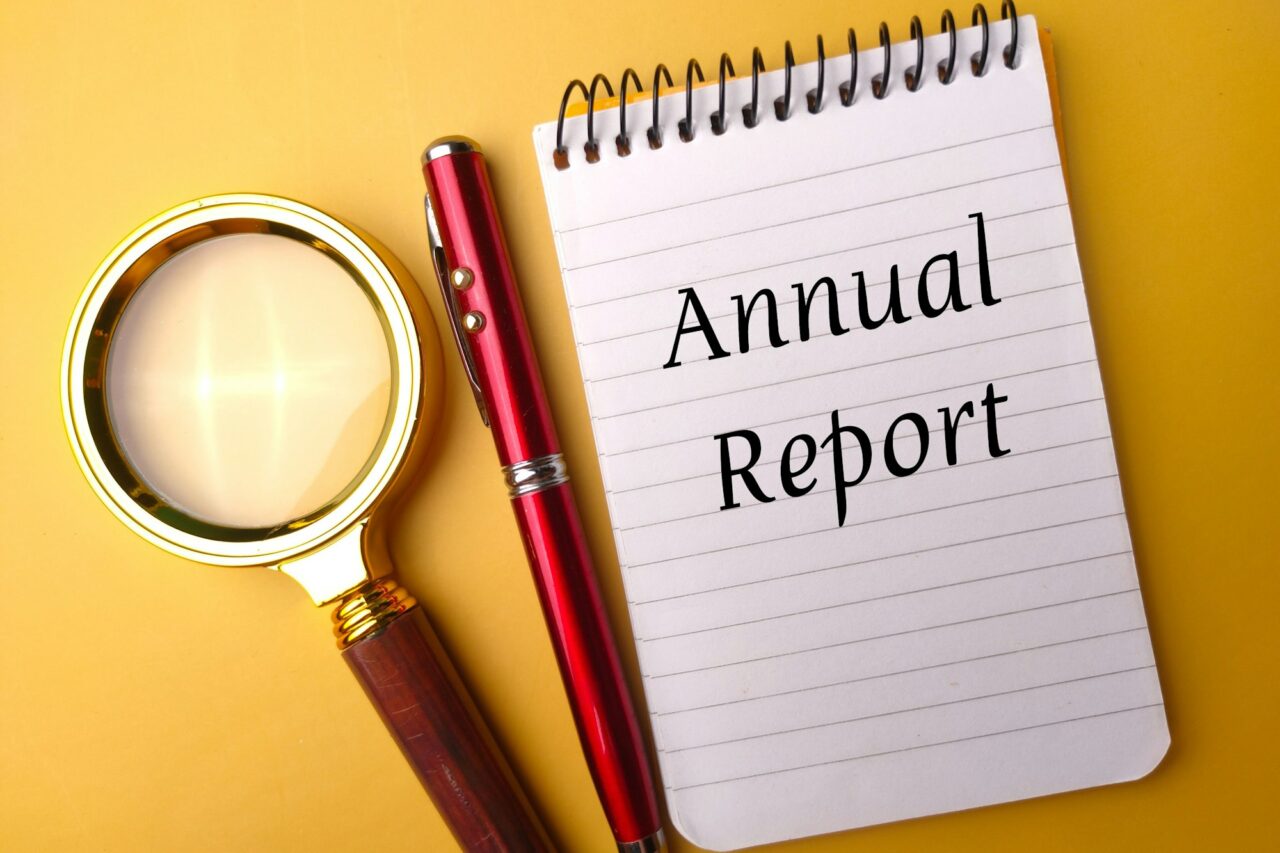 Closeup of a notepad with the text "annual report" next to a pen and a magnifying glass